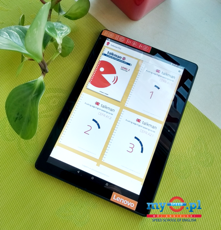 Tablet Lenovo z aplikacją edukacyjną Talkman, na tle zielonego obrusu i rośliny doniczkowej